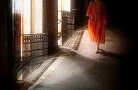 Eine Frau in rotem Kleid spaziert die Altstadt herunter, während warmes Licht aus einer Keller Galerie ihr den Weg weist. Street Fotografie von Street Fotograf Bastian Peter. Symbolbild für Artikel über Strassenfotografie in der Nacht und die Magie dabei.