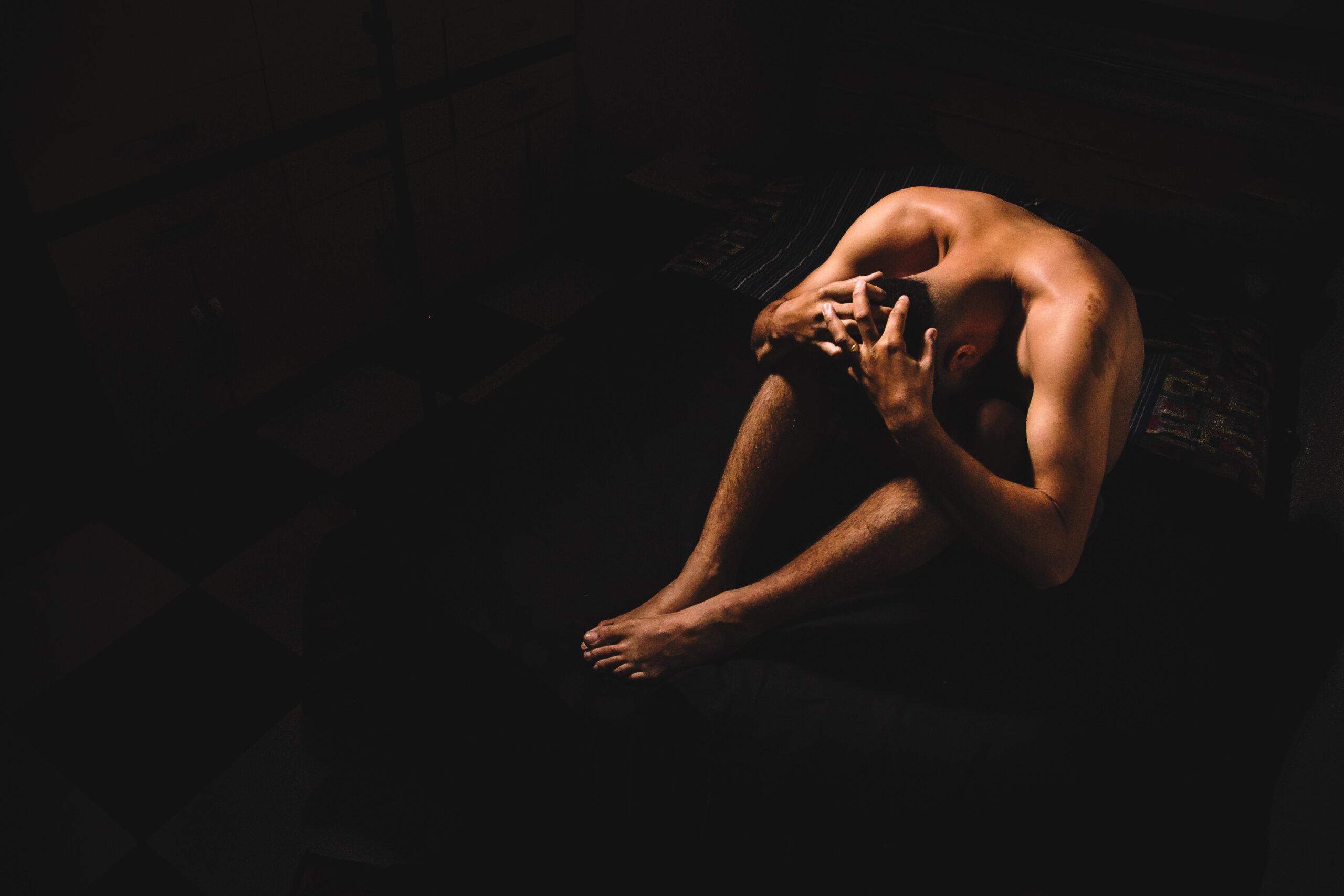 Ein Mensch sitzend am Boden, Chiarroscurro Stil. Symbolfoto zu Artikel über Akt Fotografie Mann, männliche Akt Fotografie