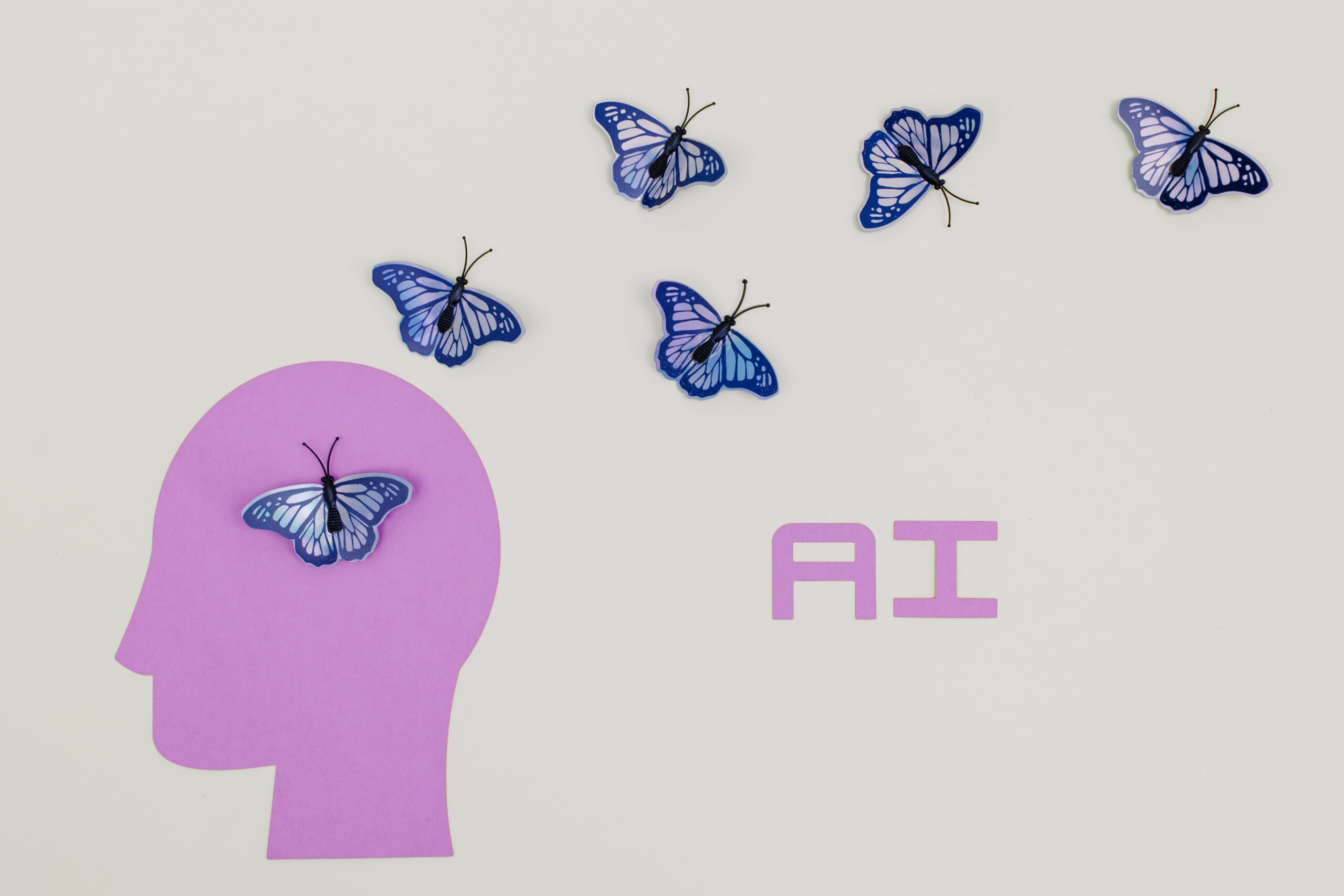 Auf grauem Hintergrund sehen wir das Symbol eines menschlichen Kopfes in violett, auf den viele blaue Schmetterlinge zufliegen. Symbolbild für Artikel: Der Aufstieg der Künstlichen Intelligenz in der Schweiz